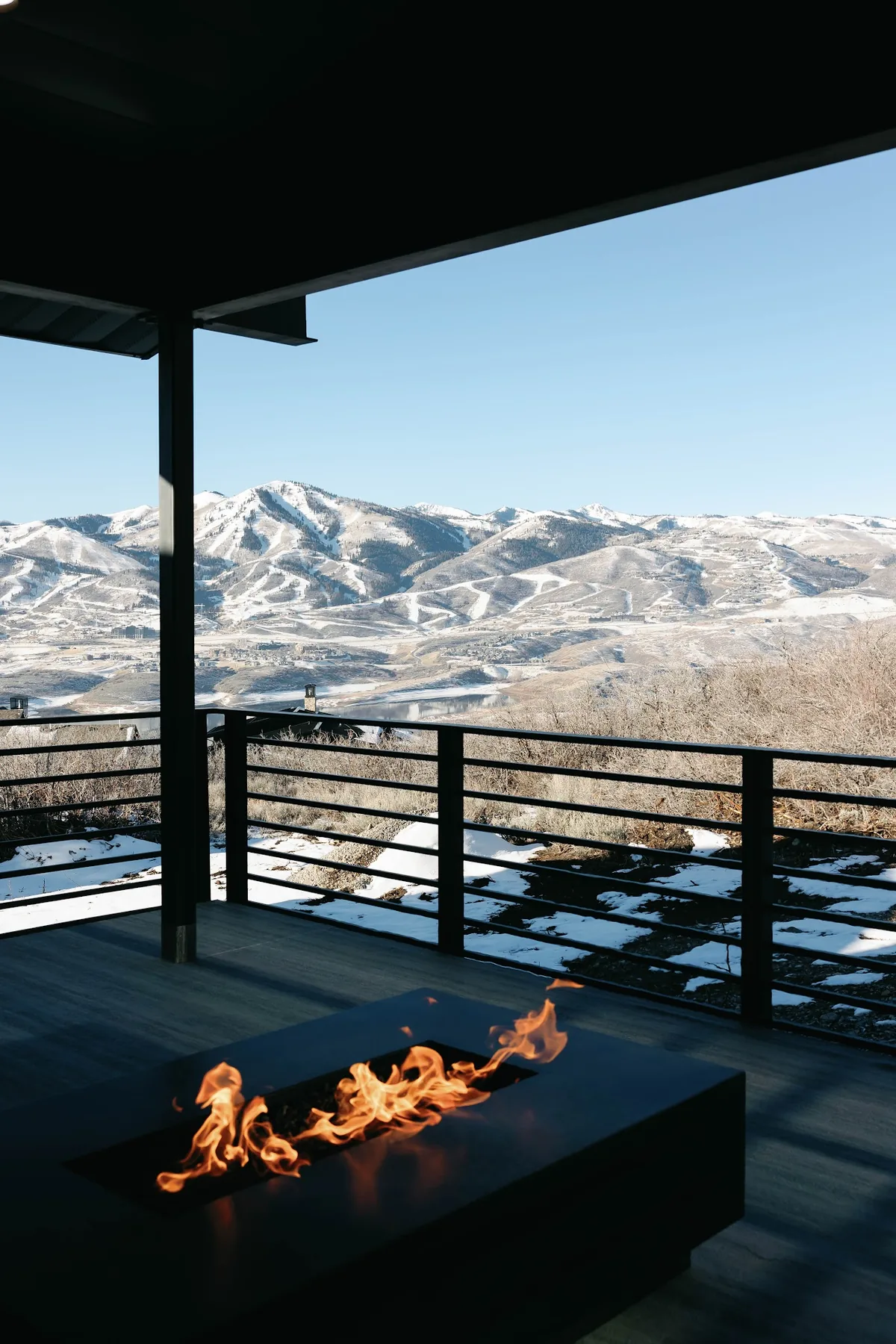 Covered deck with a linear gas fire table looking out over snow-covered Park City ski runs